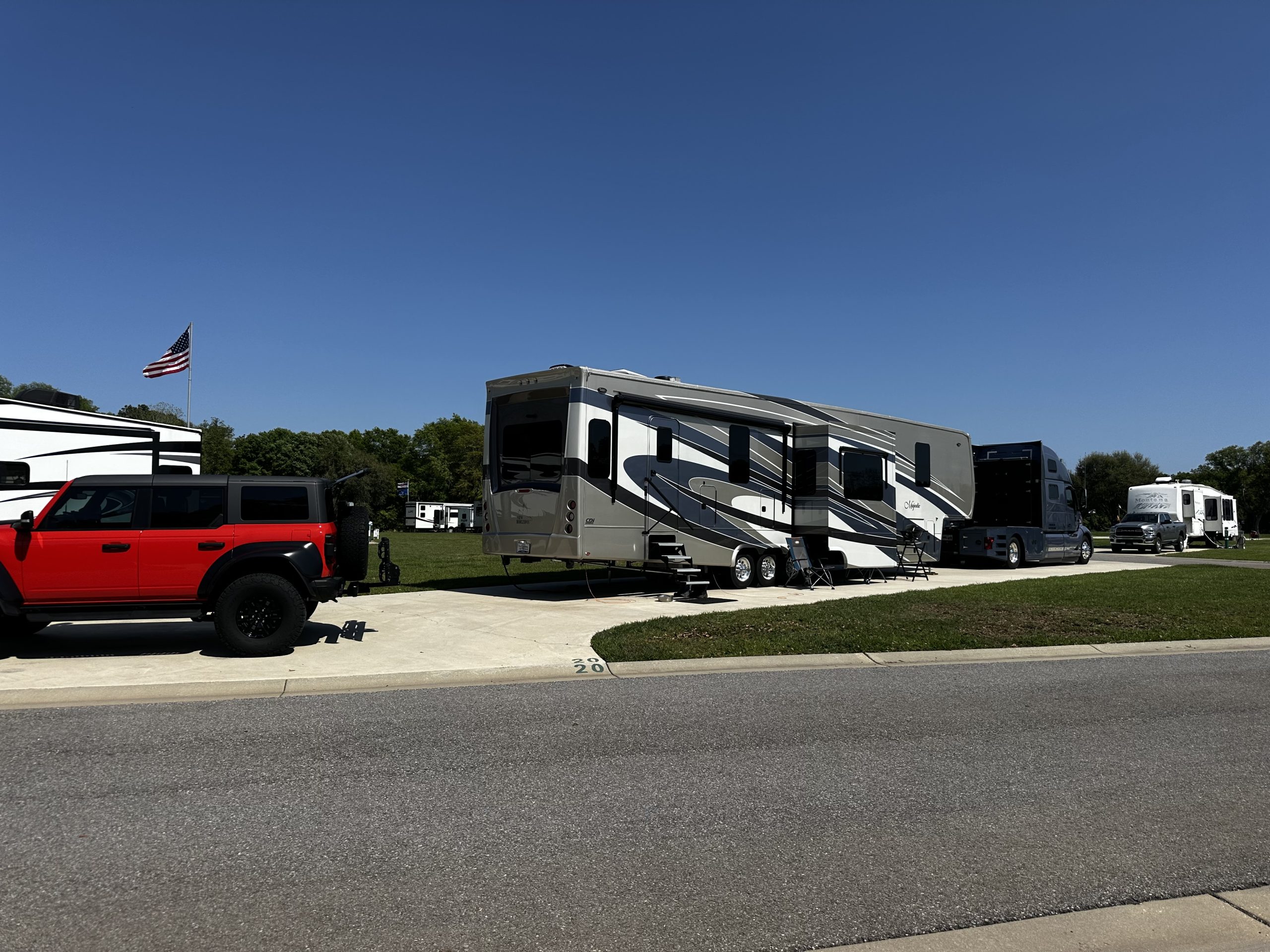 large RV and car parked in a lot at Homestead RV Comminuty